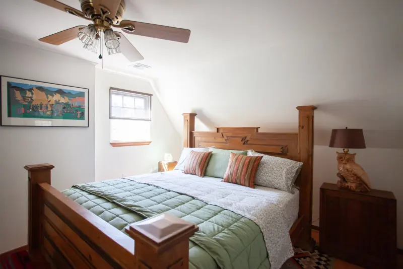 Bedroom with a carved wooden bed, green bedding and a ceiling fan