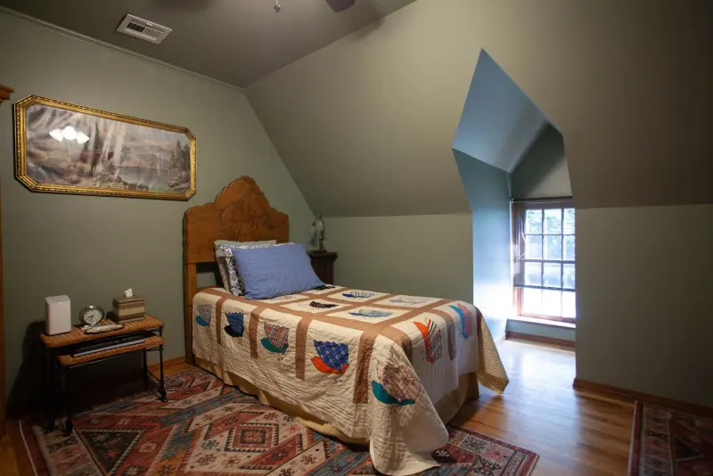Upstairs bedroom under a sloped ceiling, with a patchwork quilt and a dormer window