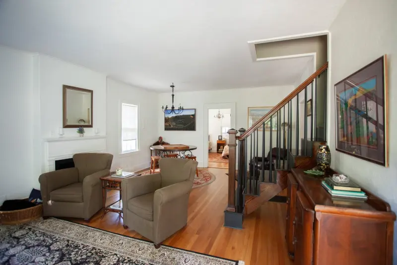 Living room with armchairs on a patterned rug, a dresser and the staircase